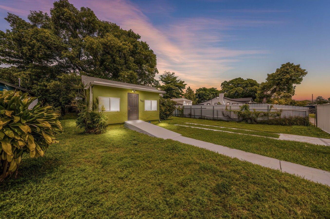 A residential property with a well-maintained lawn, a small house with a front door, and a fenced backyard.