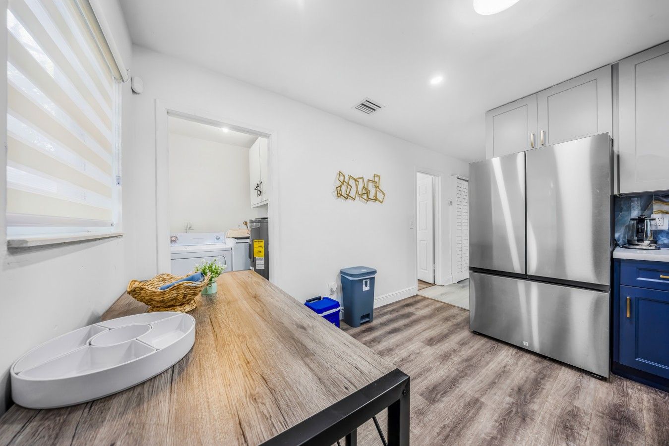 A modern kitchen with stainless steel appliances, a wooden dining table, and a blue trash bin.