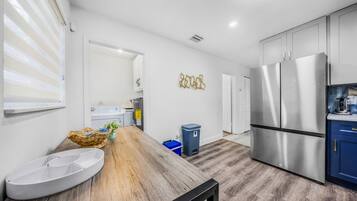 A modern kitchen with stainless steel appliances, a wooden dining table, and a blue trash bin.