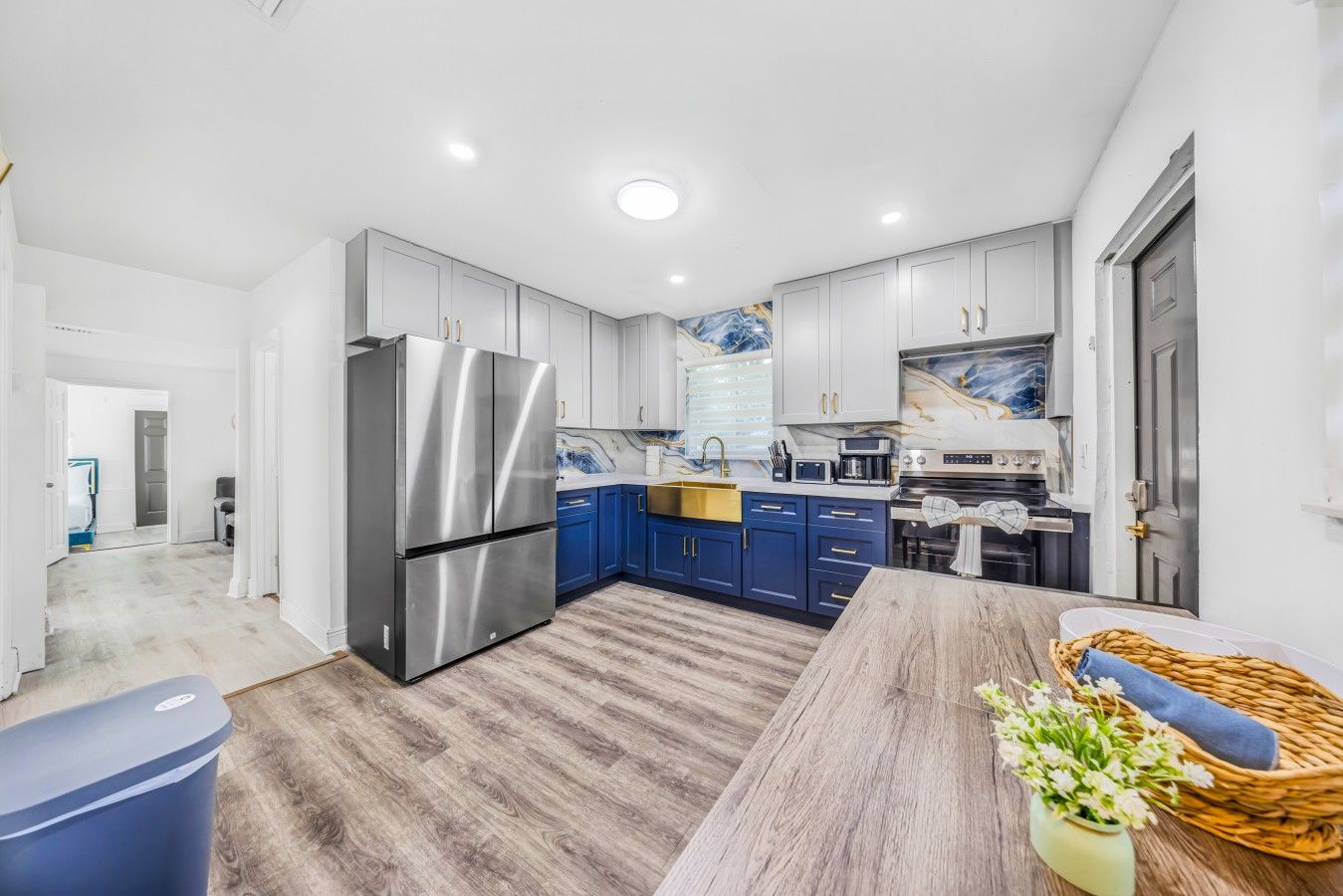 A modern kitchen with stainless steel appliances, blue cabinets, and a wooden floor.