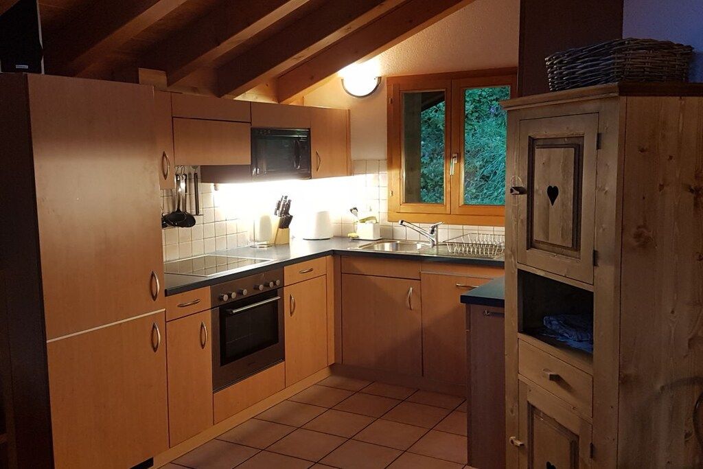 Une cuisine avec des meubles de rangement en bois, un poêle noir et une fenêtre donnant sur un paysage verdoyant.