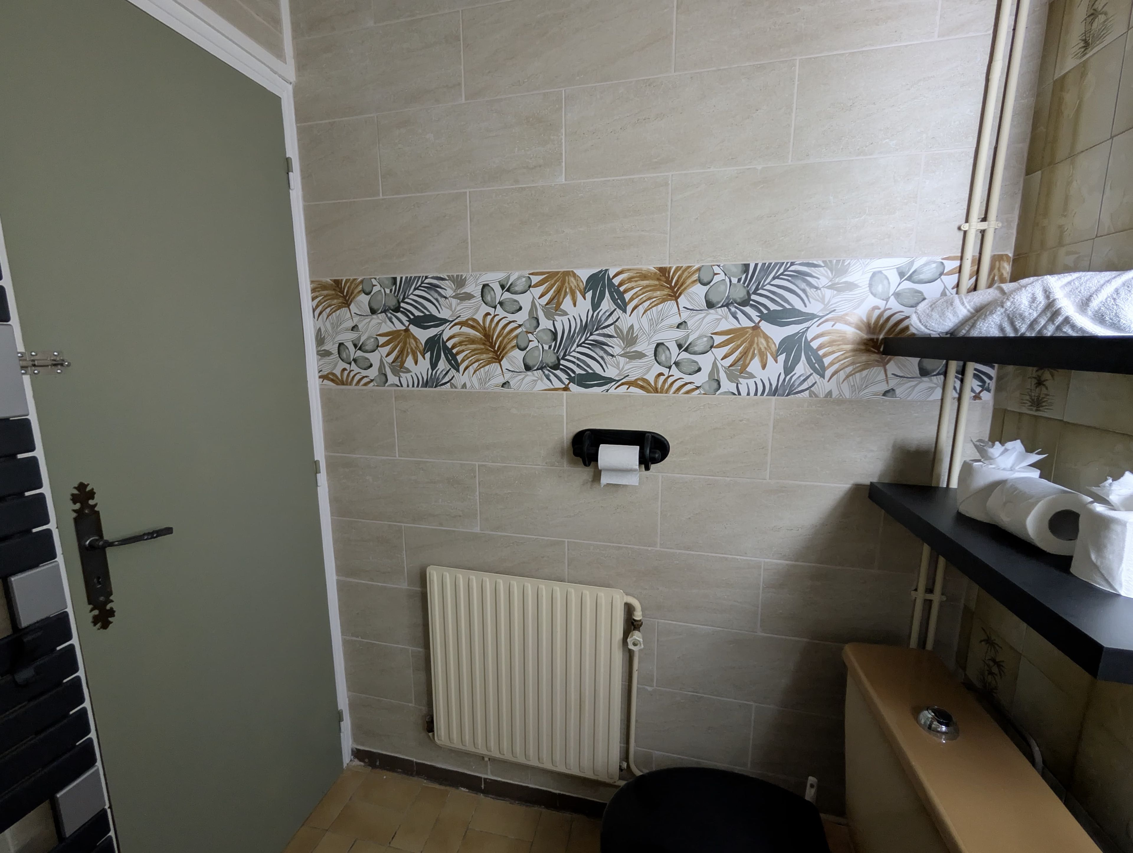 Une salle de bain équipée de toilettes, d’un radiateur et d’une étagère où sont rangés les articles de toilette.