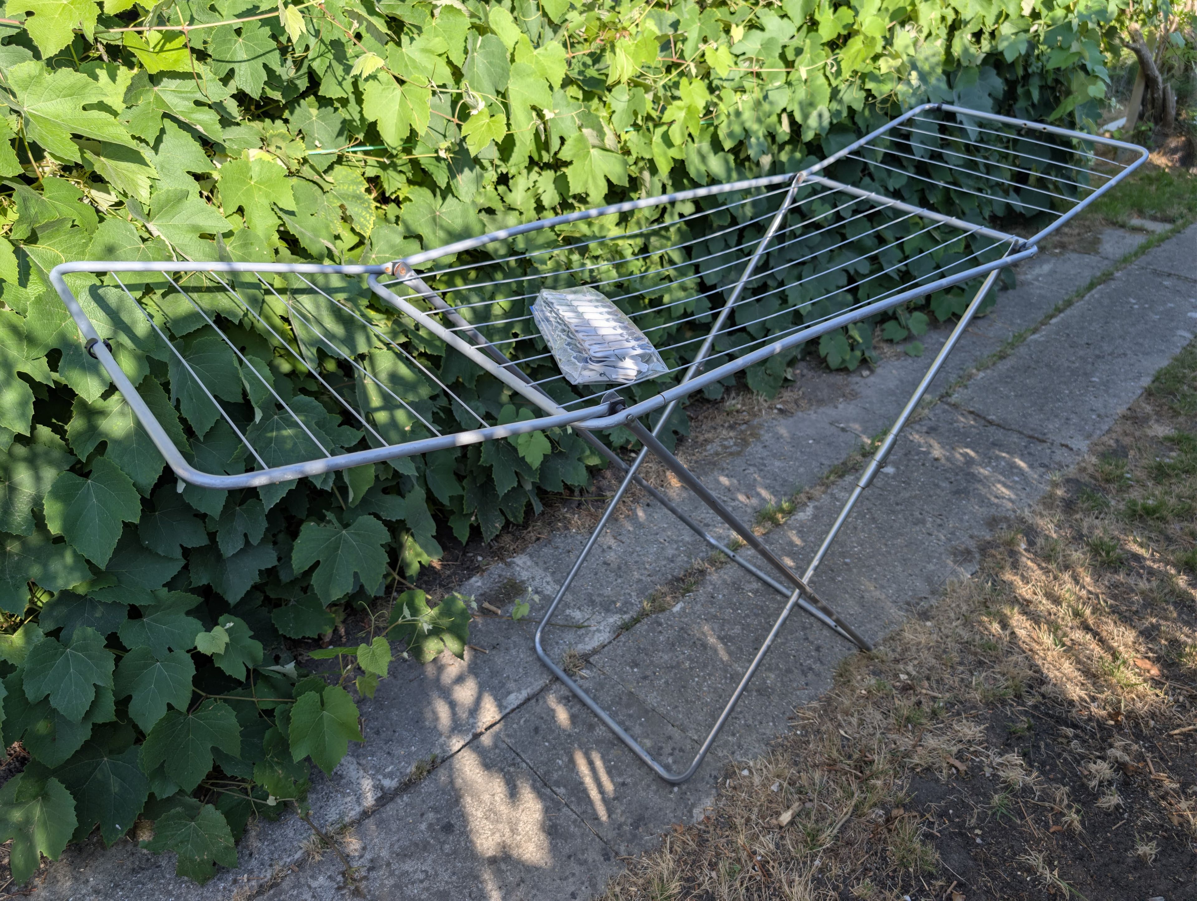 A metal drying rack with a folded towel on a concrete surface next to a hedge.