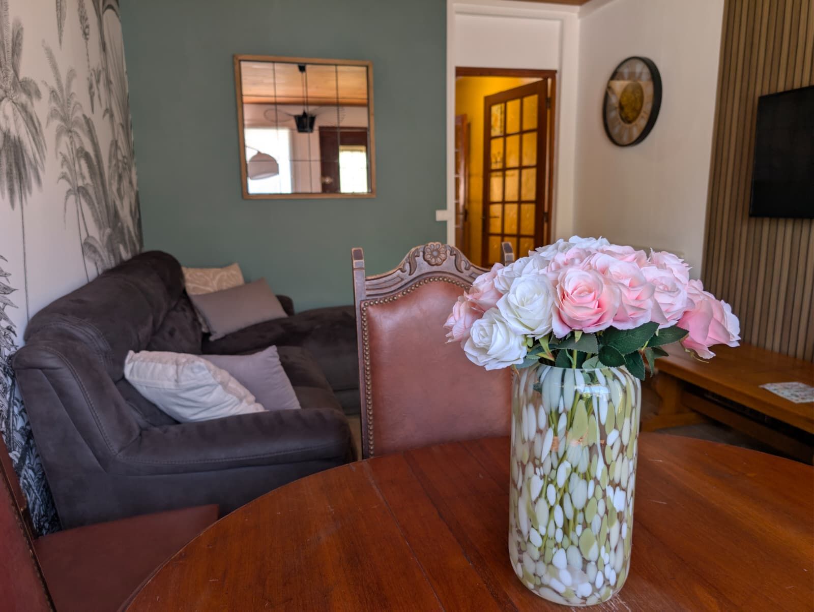 A living room with a brown leather sofa, a wooden coffee table, and a vase with pink and white flowers.