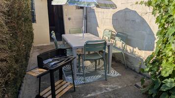 An outdoor patio with a table and chairs, a striped umbrella, and a grill cart.