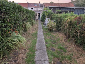 Un camí estret flanquejat per vegetació densa i edificis residencials.