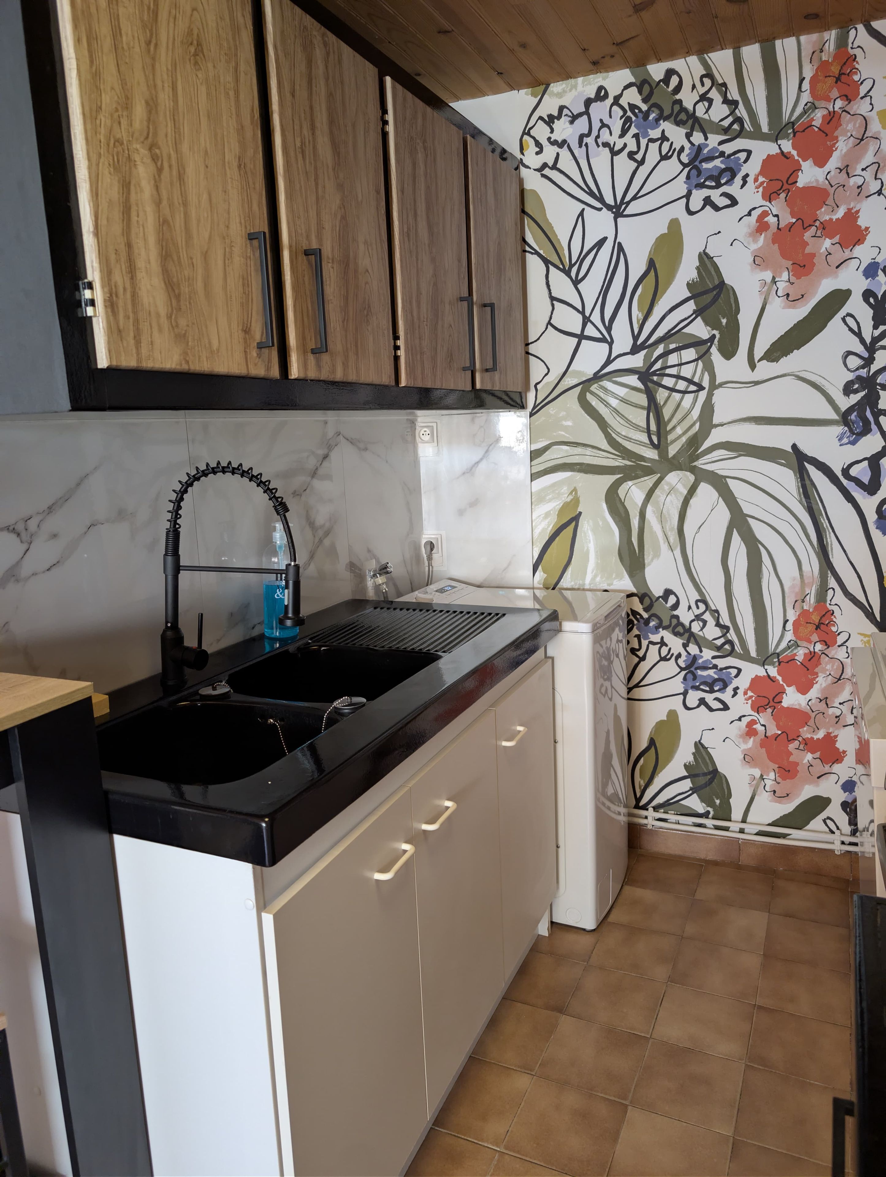 Eine Küche mit einem schwarzen Spülbecken, Holzschränken und einem Wanddesign mit floralem Muster.