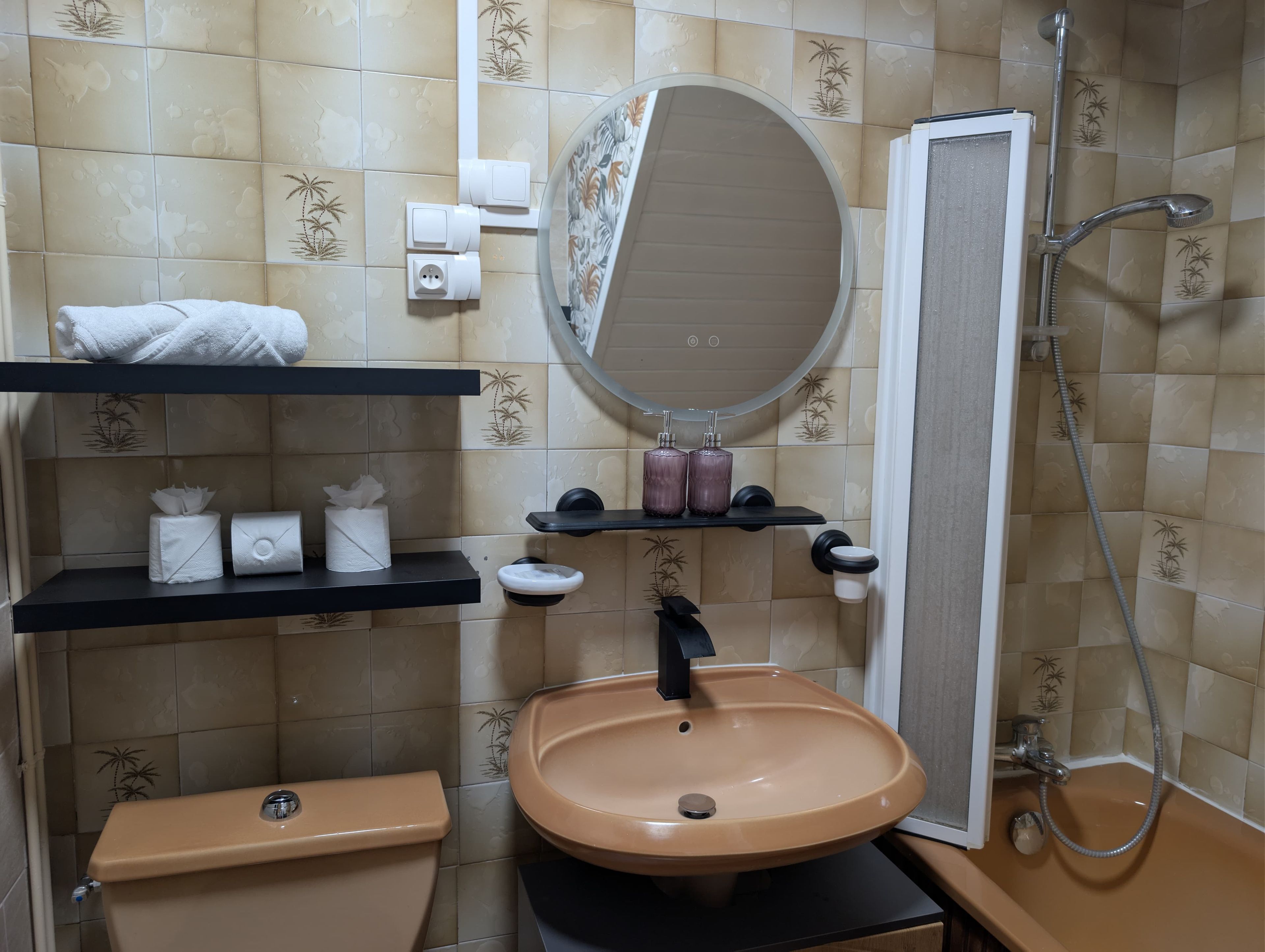 A bathroom with a beige sink, toilet, and shower. There are shelves with towels and toiletries.