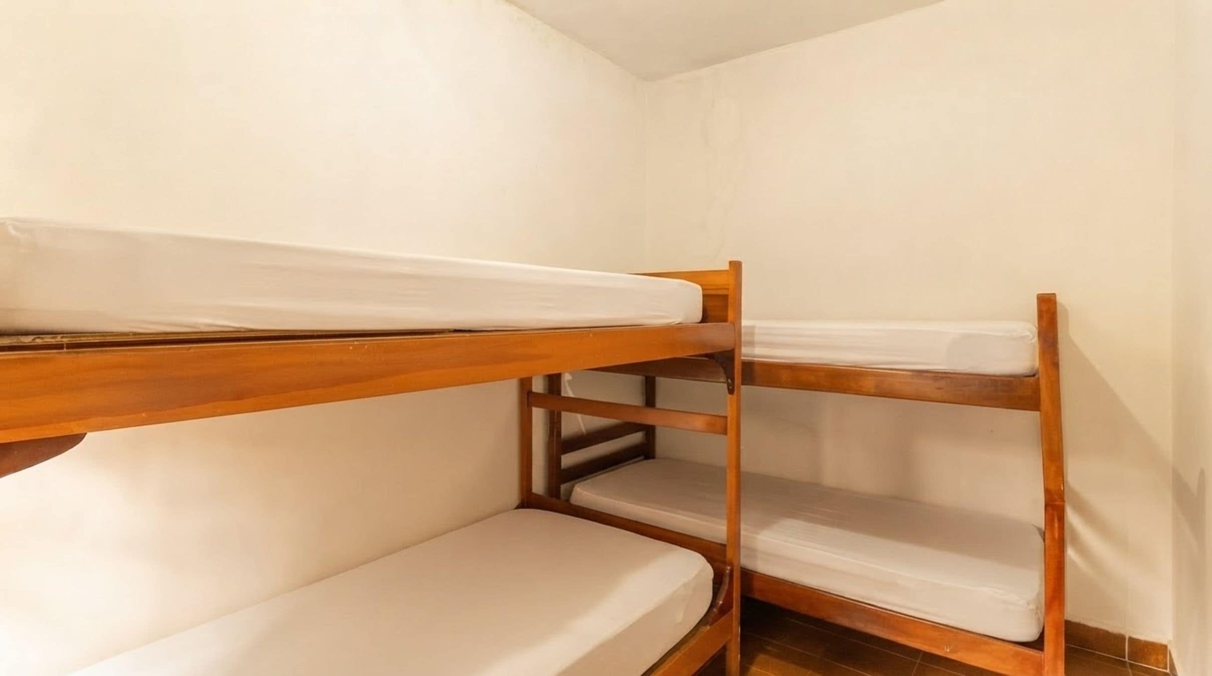 Une chambre avec un lit superposé, dont les structures sont en bois et la literie est blanche.