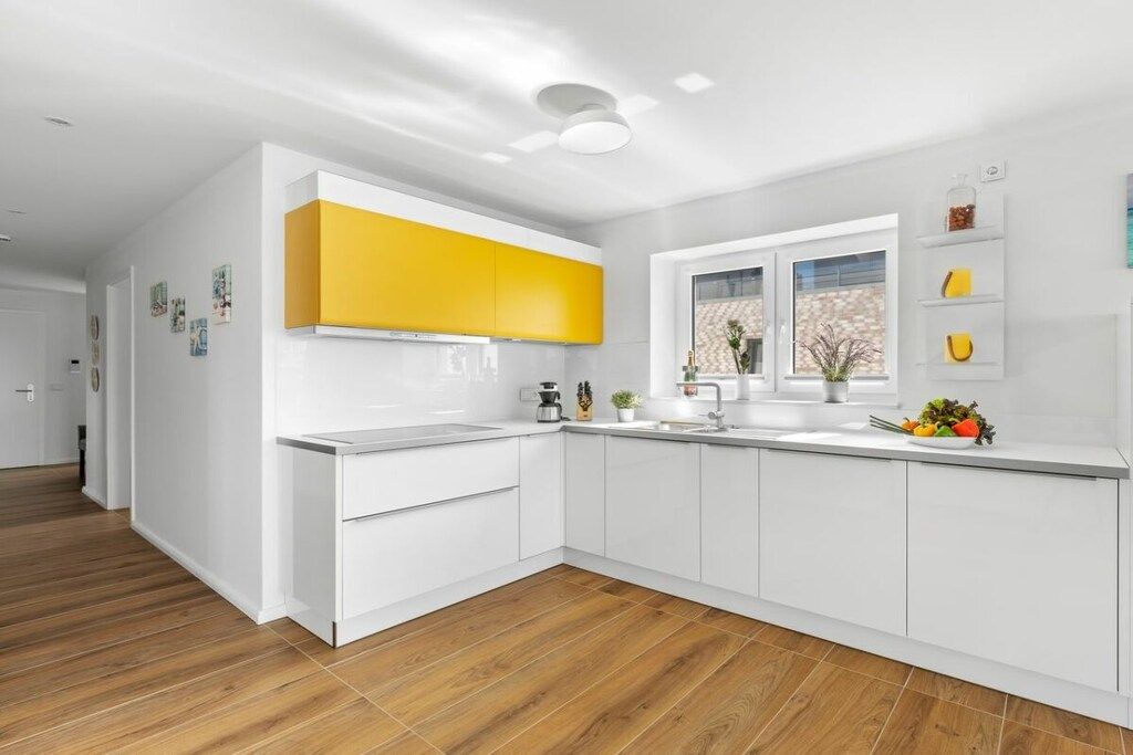 Une cuisine moderne avec des meubles blancs, un mur d’accent jaune et une fenêtre offrant une belle vue.