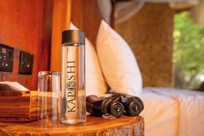 Eine klare Flasche mit dem Aufdruck 'KAPOSHI', ein Fernglas und ein Glas auf einer Holztischplatte.