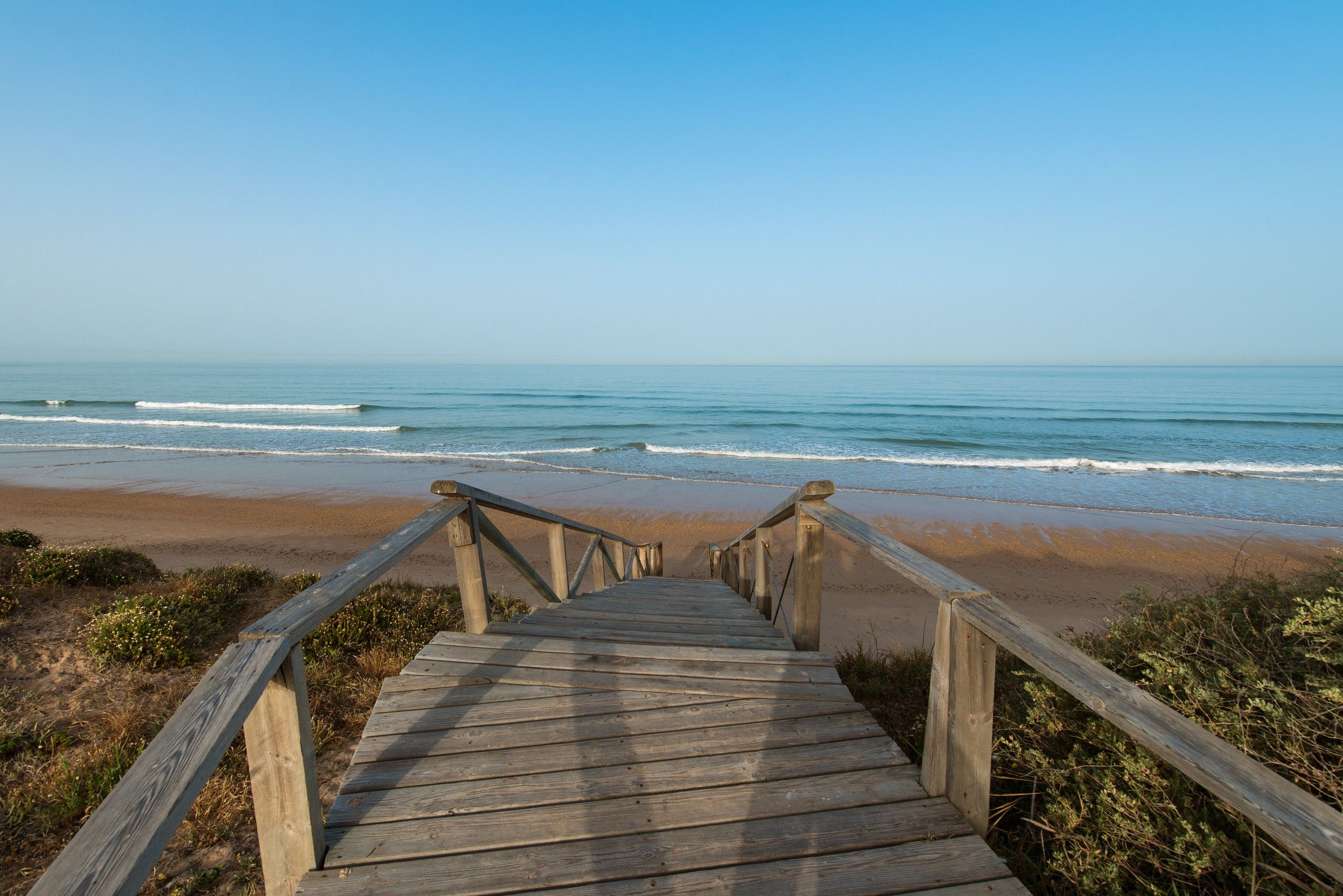 A wooden staircase leading to a beach with a clear view of the ocean.