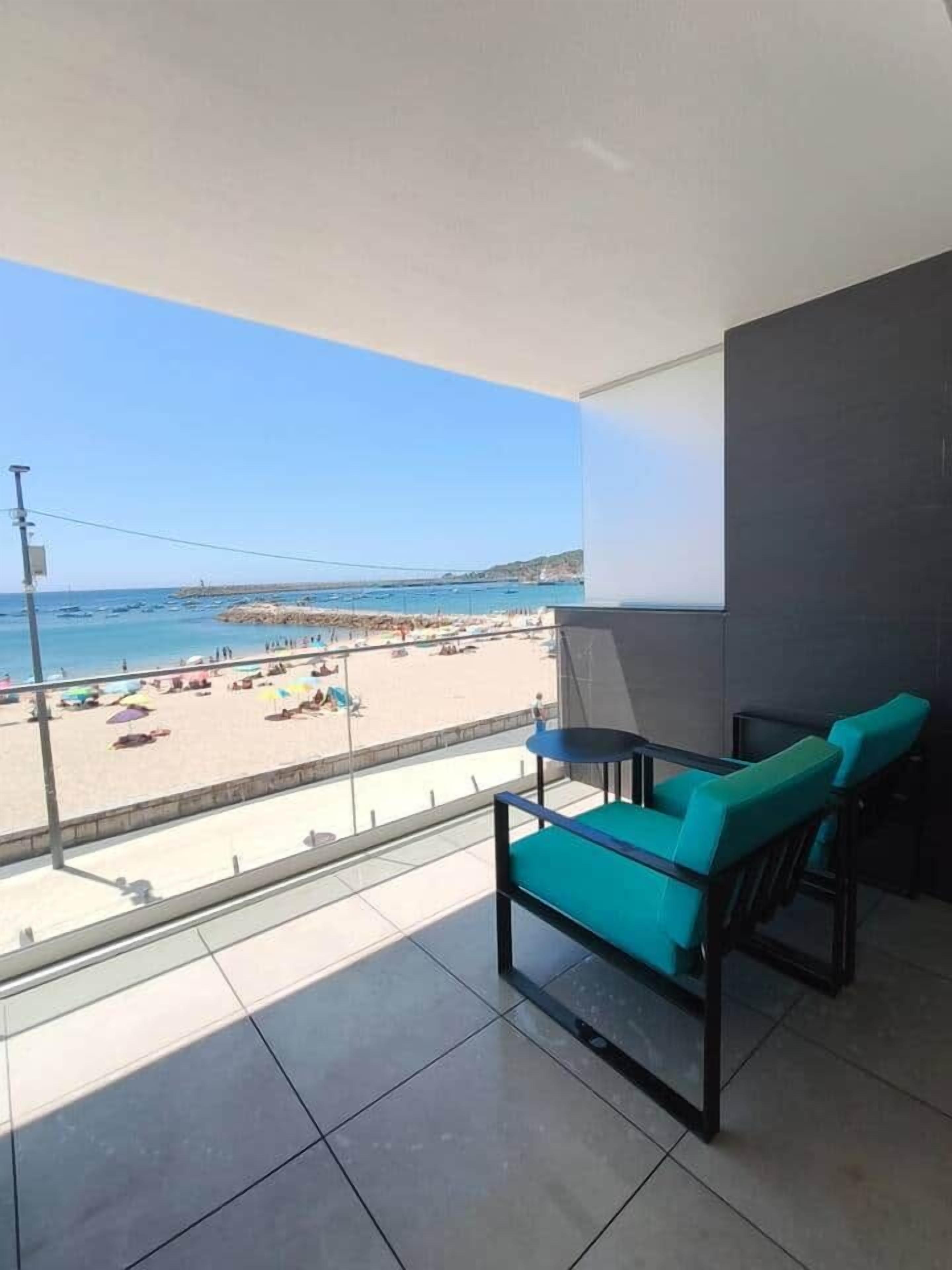 A balcony with a view of a beach, a table, and two chairs.
