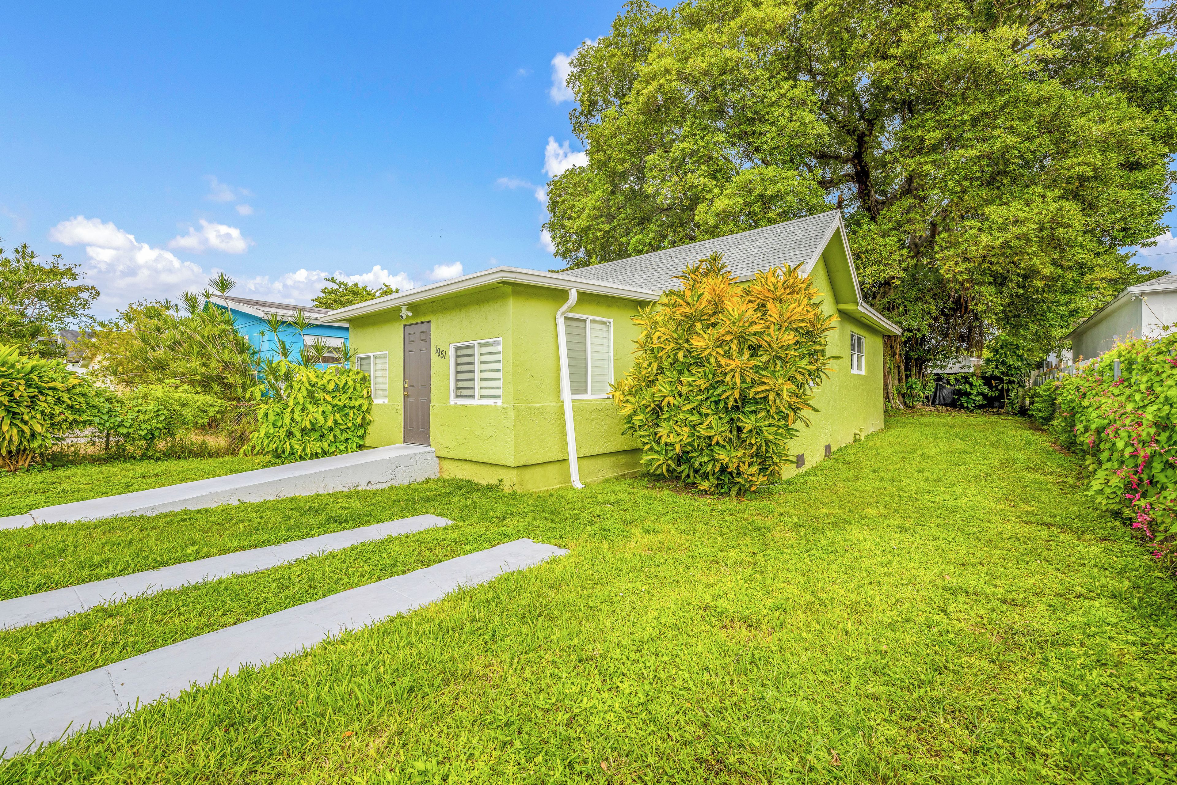 A small, single-story house with a green exterior, a front porch, and a well-maintained lawn.