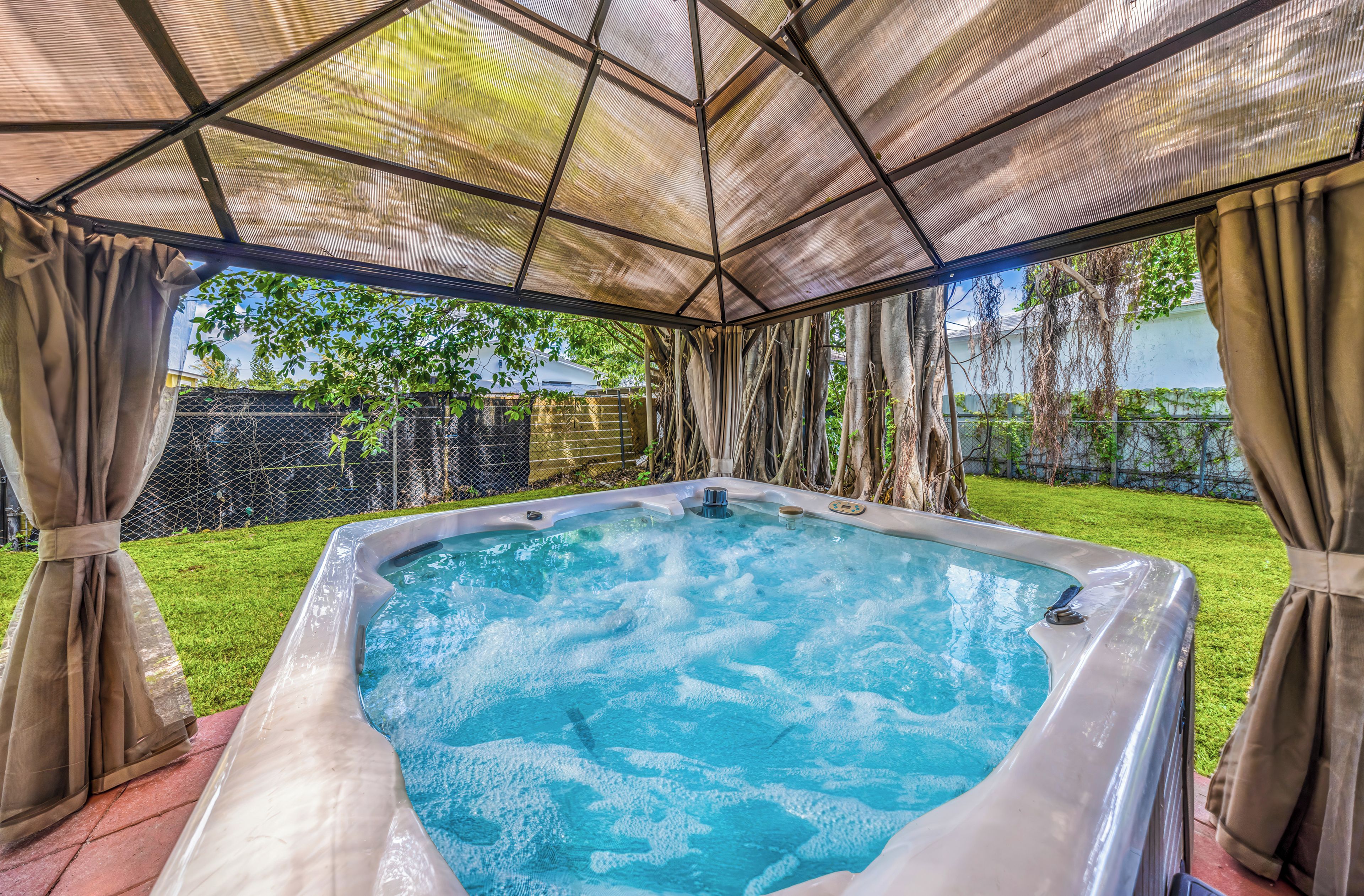 Un jacuzzi bajo un porche cubierto con vista a un patio trasero.