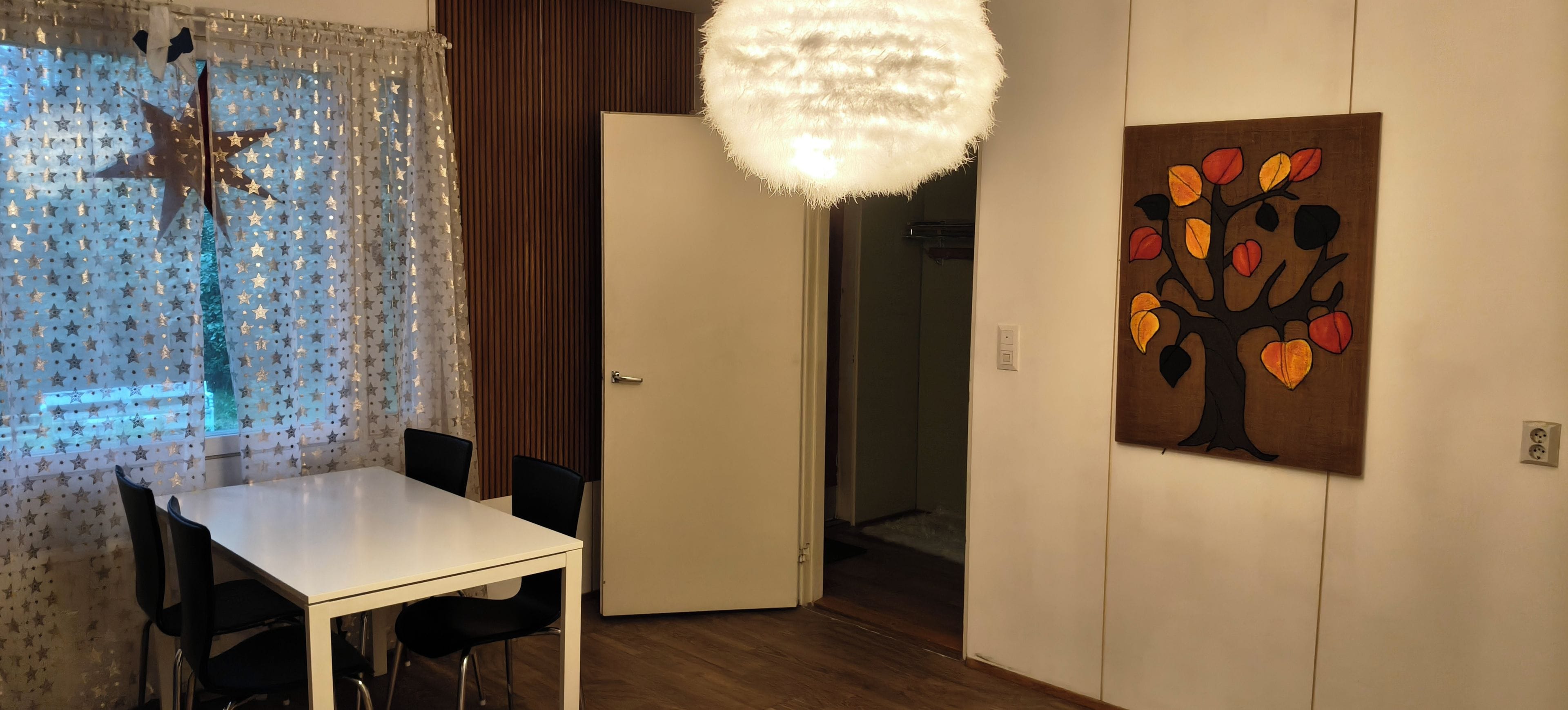 A room with a white table and chairs, a door, a wall-mounted painting, and a hanging light fixture.