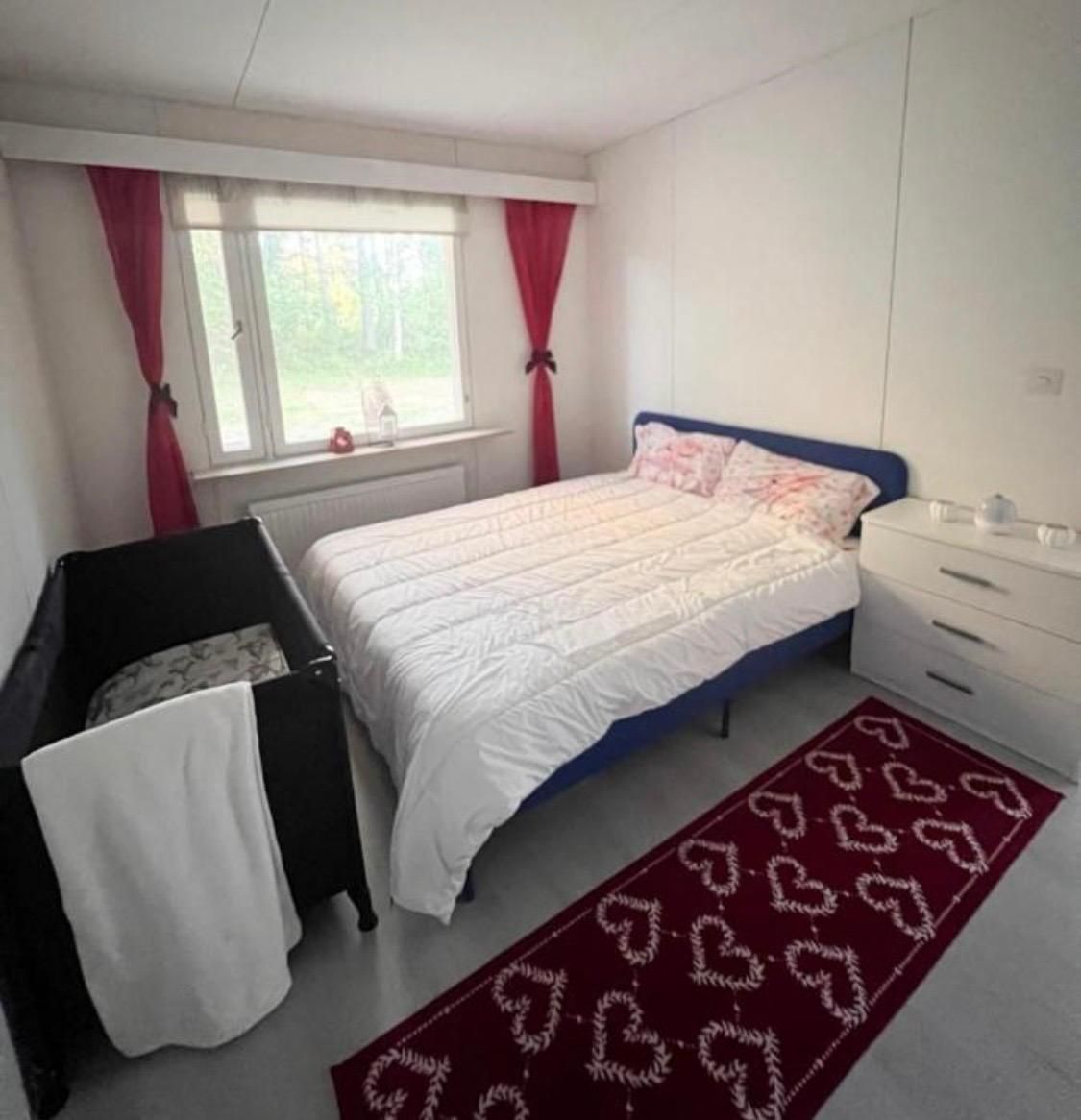A bedroom with a bed, a nightstand, a dresser, and a window with curtains.