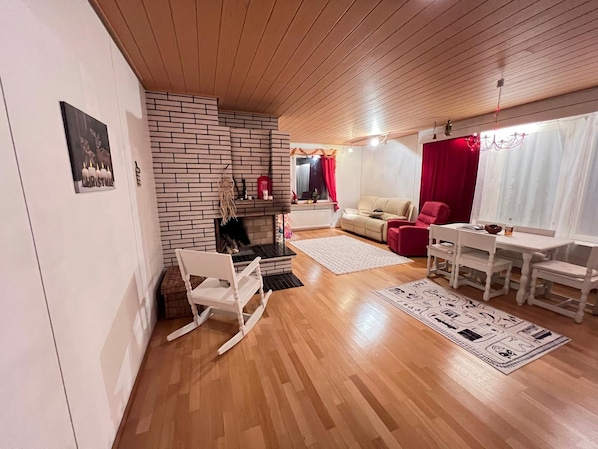 A cozy living room with a brick fireplace, a sofa, a red chair, a dining table with chairs, and a white rocking chair. - Stay with your guide in Rovaniemi area, Perfect for local experience. (Rovaniemi)