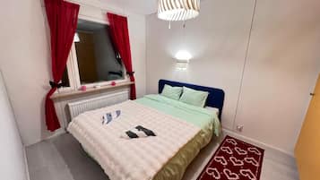 A bedroom with a bed, a window with red curtains, a bedside lamp, and a patterned rug.