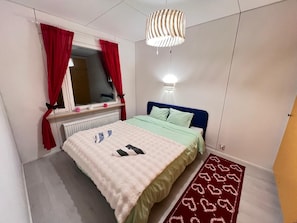 A bedroom with a bed, a window with red curtains, a bedside lamp, and a patterned rug. - Stay with your guide in Rovaniemi area, Perfect for local experience. (Rovaniemi)