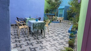 An outdoor patio with a table and chairs, surrounded by potted plants and a patterned floor.