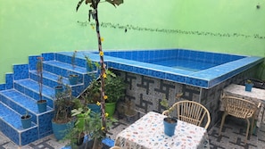 A small outdoor area with a blue tiled pool, steps leading up to it, and a table with chairs.
