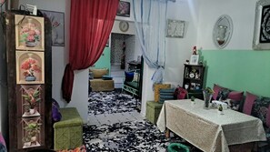 A cozy living room with a patterned rug, a green sofa, a table with a vase, and a bookshelf.