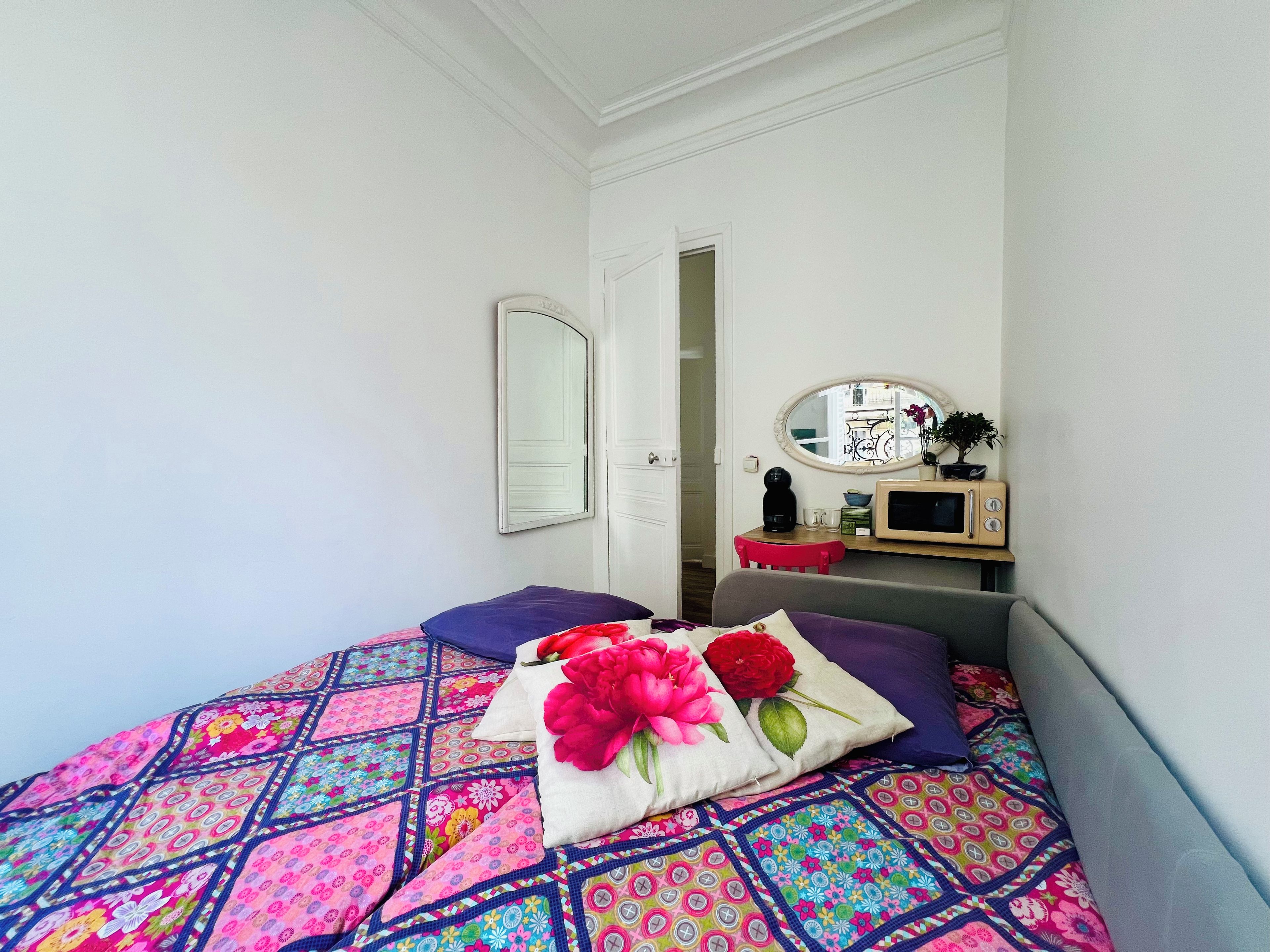 Une chambre à coucher avec un lit, des oreillers, une table de chevet, un miroir et une porte donnant sur une autre pièce.
