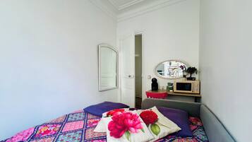 Une chambre à coucher avec un lit, des oreillers, une table de chevet, un miroir et une porte donnant sur une autre pièce.