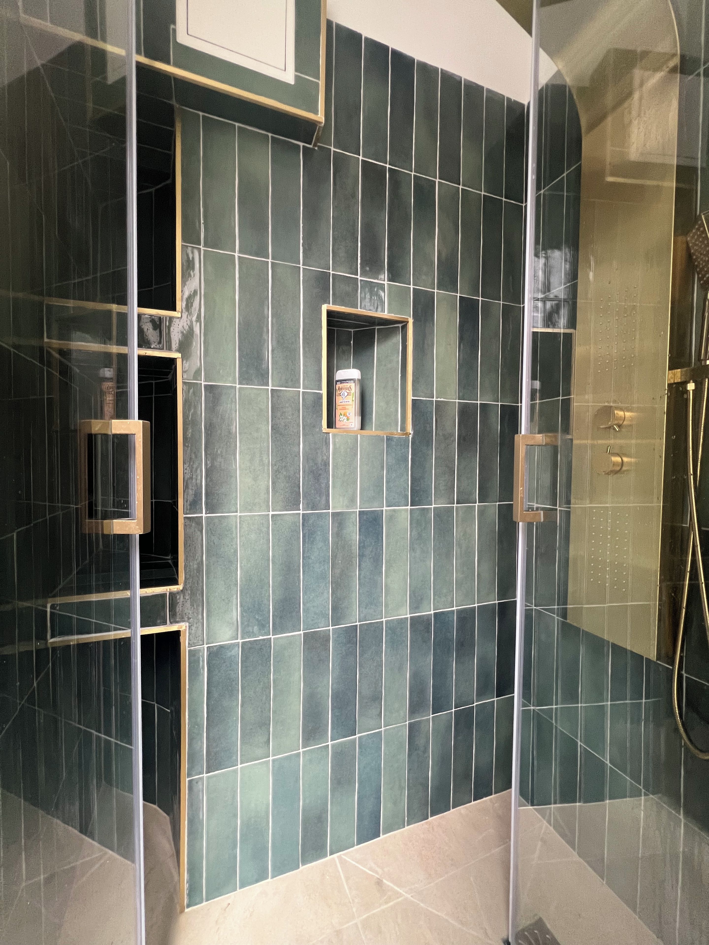 Een moderne badkamer met een douchecabine van glas, een ingebouwd schapje met toiletartikelen en een betegelde wand.