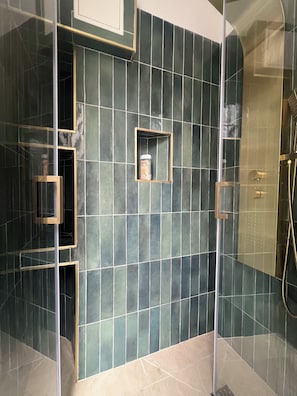 Un baño moderno con cabina de ducha de vidrio, estante empotrado con artículos de tocador y pared revestida de azulejos.