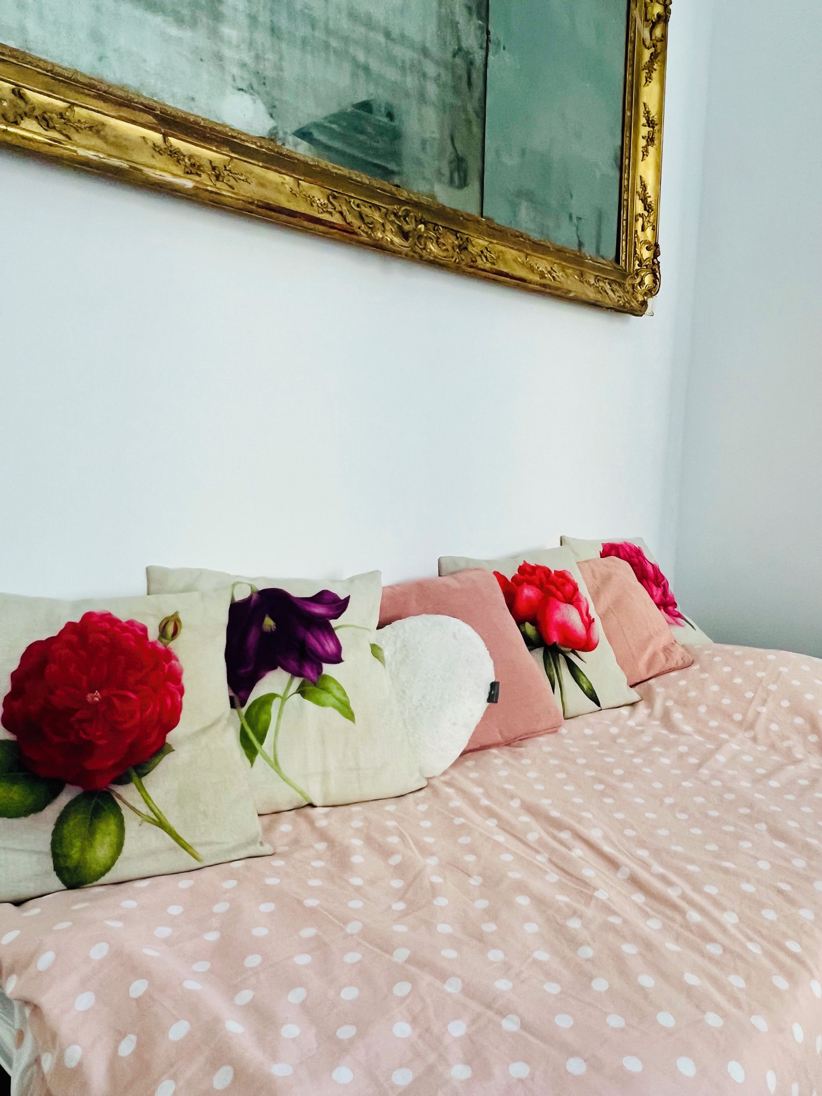 Een bed met een stippenhoes en decoratieve kussens met bloemmotieven.