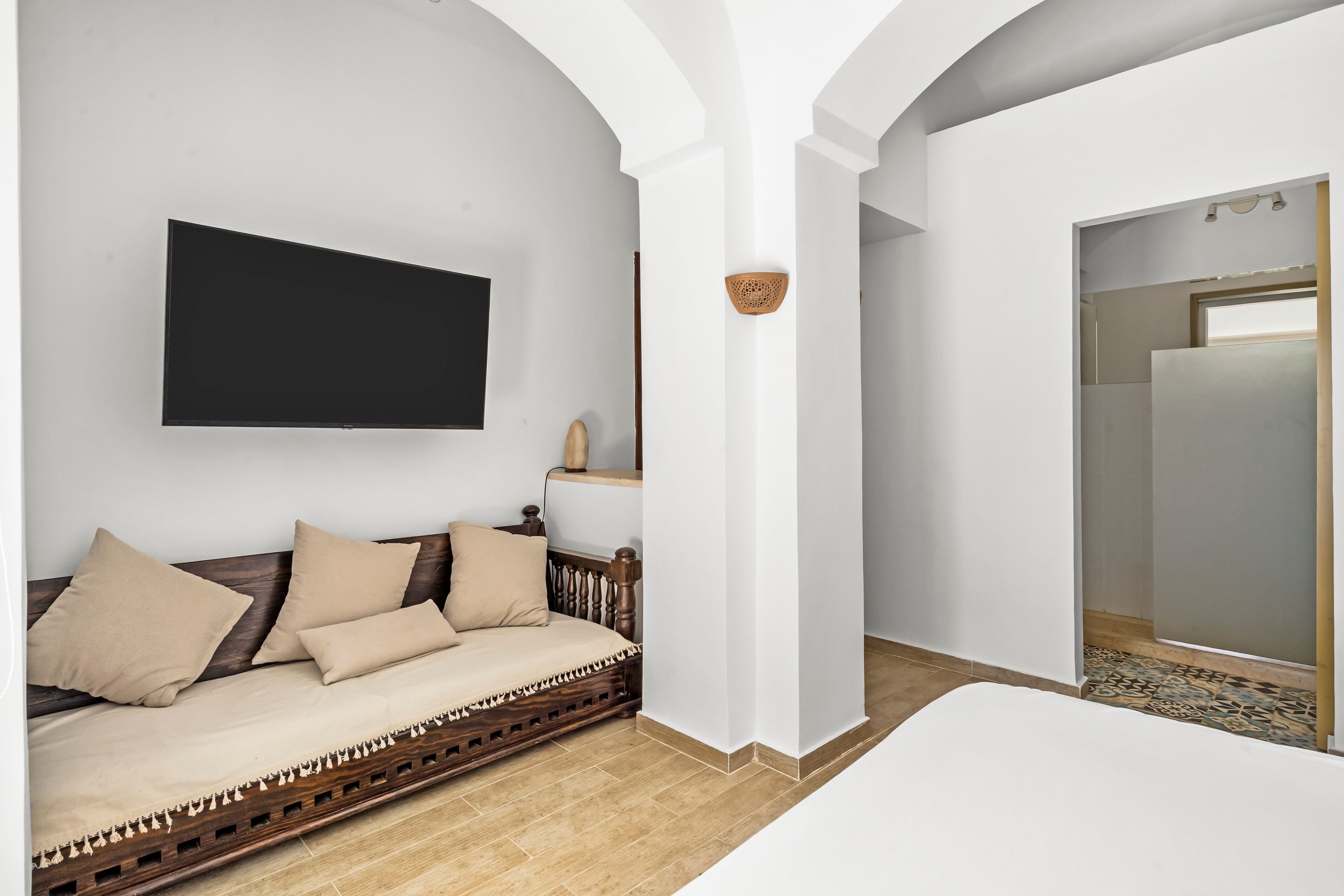 A modern room with a sofa, a flat-screen TV, a wooden-framed mirror, and a patterned floor.
