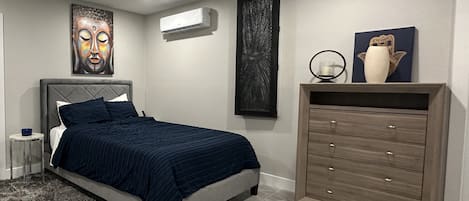 A bedroom with a bed, a dresser, a wall-mounted air conditioner, and a ceiling fan.