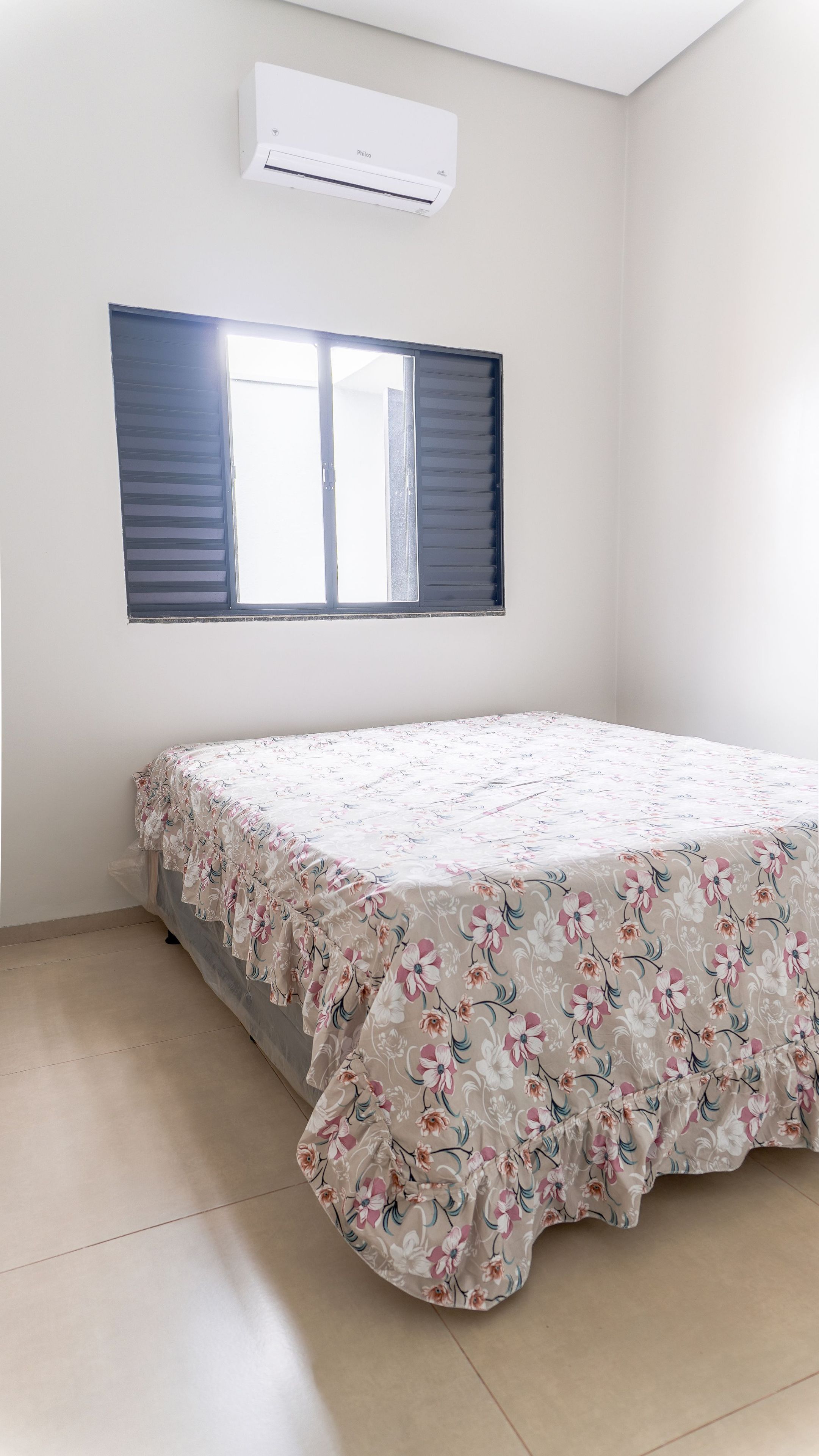 Une chambre à coucher avec un lit, un climatiseur et une fenêtre avec des stores.