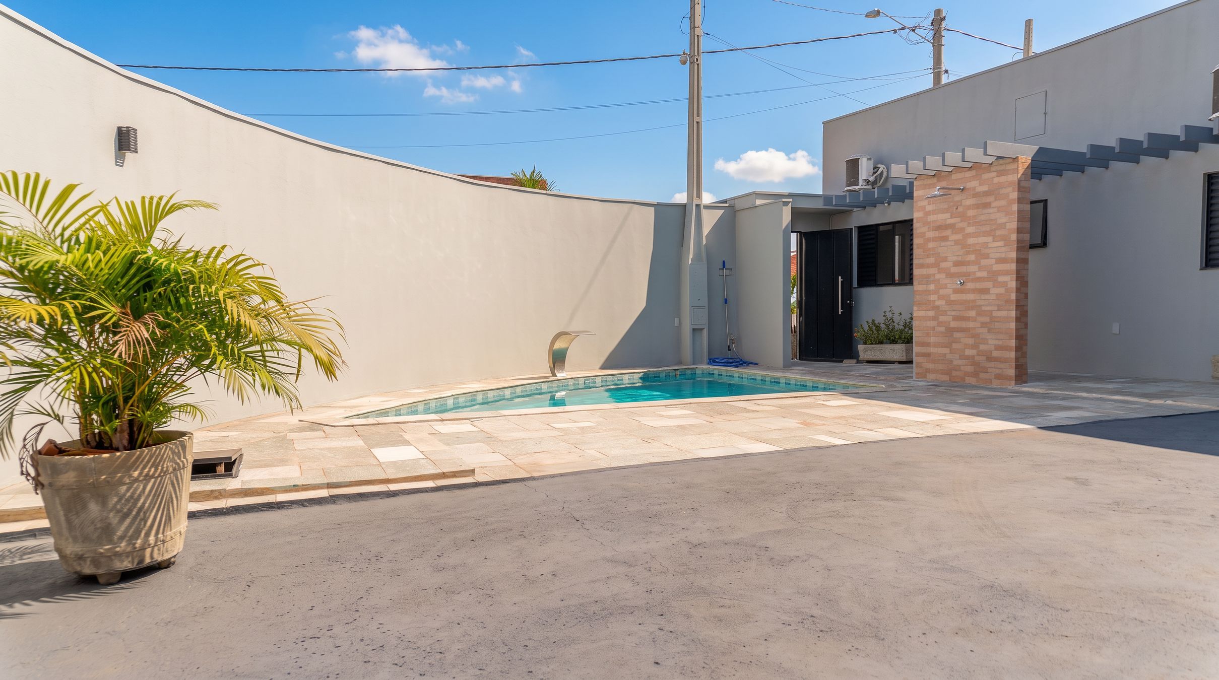 A swimming pool with a tiled deck, a potted plant, and a modern building with a staircase.