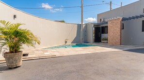 A swimming pool with a tiled deck, a potted plant, and a modern building with a staircase.