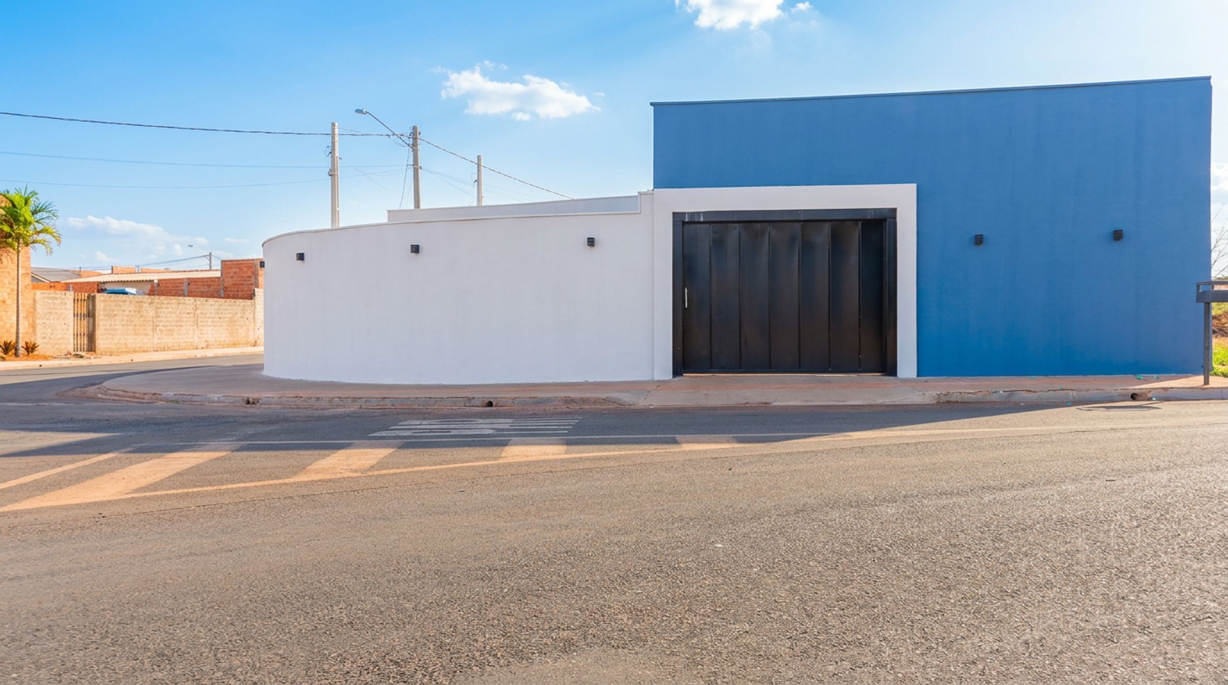 A modern building with a white and blue facade, a gated entrance, and a paved road in front.