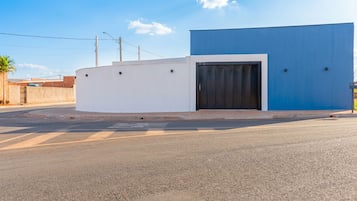 A modern building with a white and blue facade, a gated entrance, and a paved road in front.