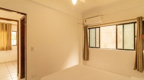 A room with a large window, a ceiling fan, and a door leading to another room. - Apartment with BBQ and Garage in Praia Grande (Ubatuba)
