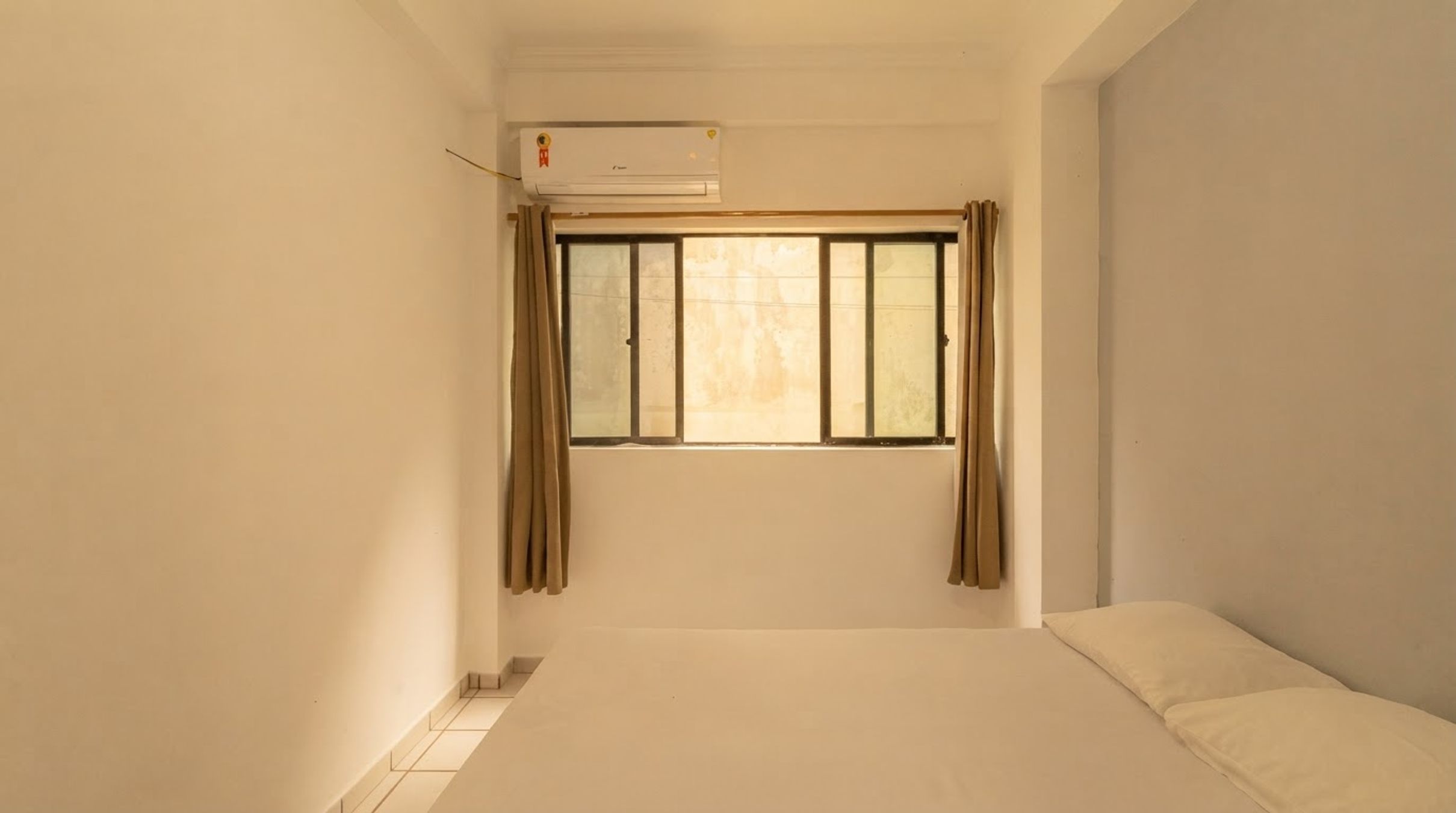 A room with a single bed, a window with curtains, and an air conditioning unit.