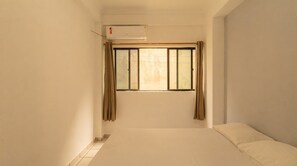 Habitació amb un llit individual, una finestra amb cortines i un aparell d'aire condicionat.