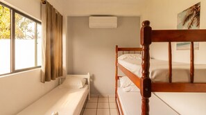 Ein Zimmer mit einem Etagenbett, einem Einzelbett und einem Fenster mit Vorhängen.