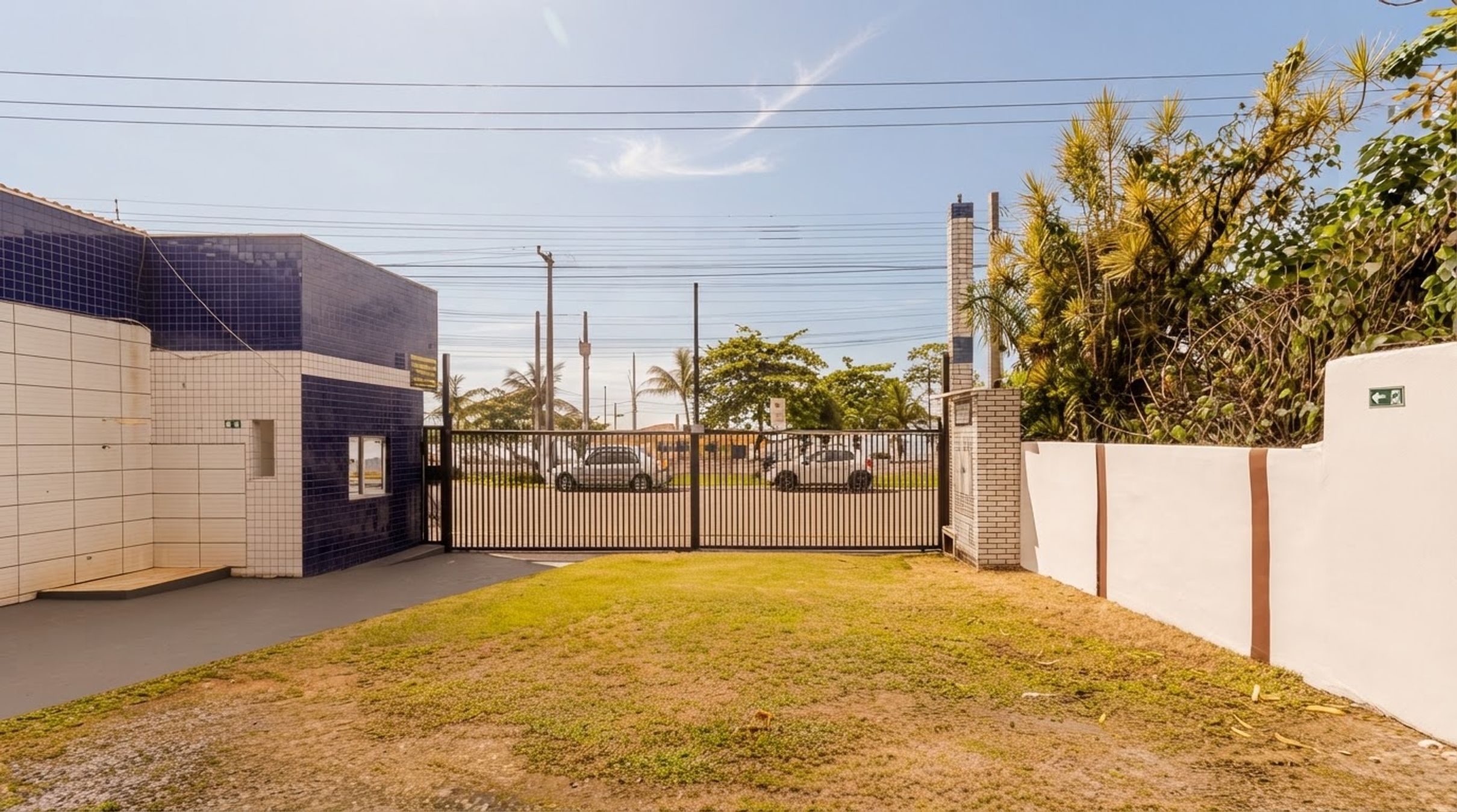 A gated property with a paved driveway, a small grassy area, and a building with tiled walls.