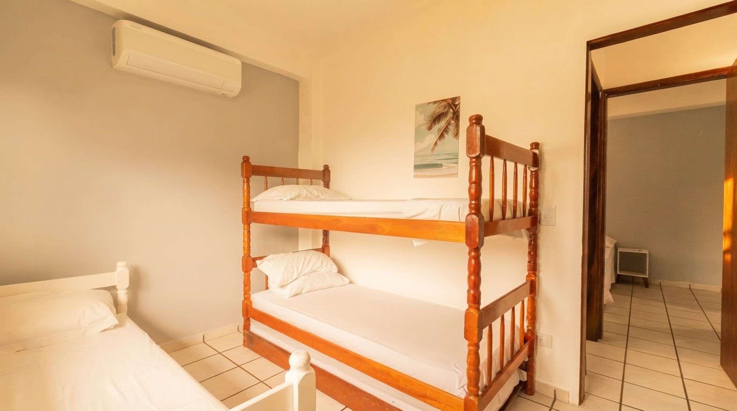A room with a bunk bed, a single bed, a wall-mounted air conditioner, and a small picture.