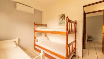 A room with a bunk bed, a single bed, a wall-mounted air conditioner, and a small picture.