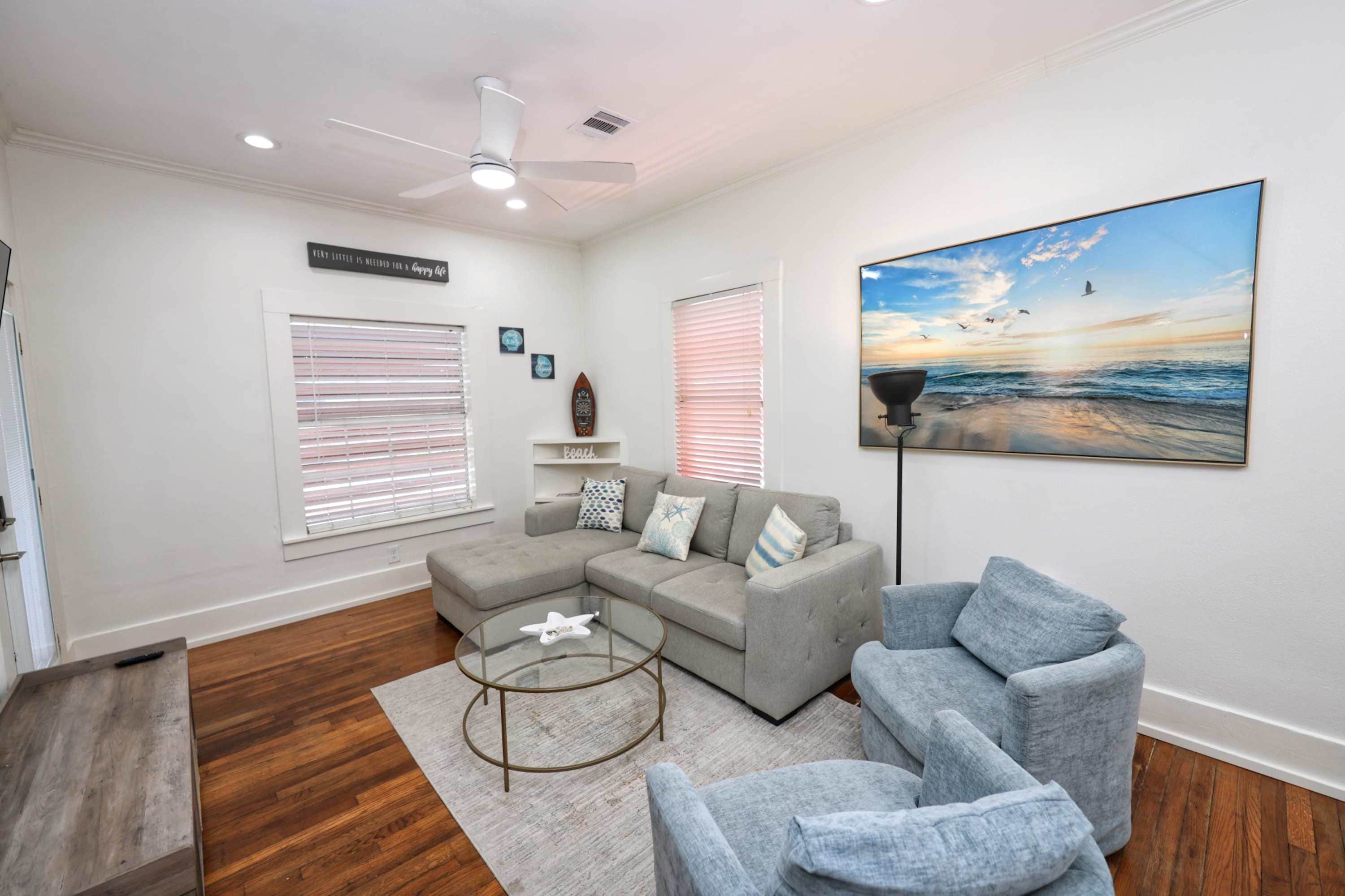 A living room with a sectional sofa, a round coffee table, and a beach-themed painting.