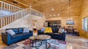 A wooden interior with a staircase, two sofas, a dining table, and a kitchen area. - Chill N in the Smokies 2-Bdrm & Loft, Hot Tub, Game Tables & Resort Pool (Gatlinburg)