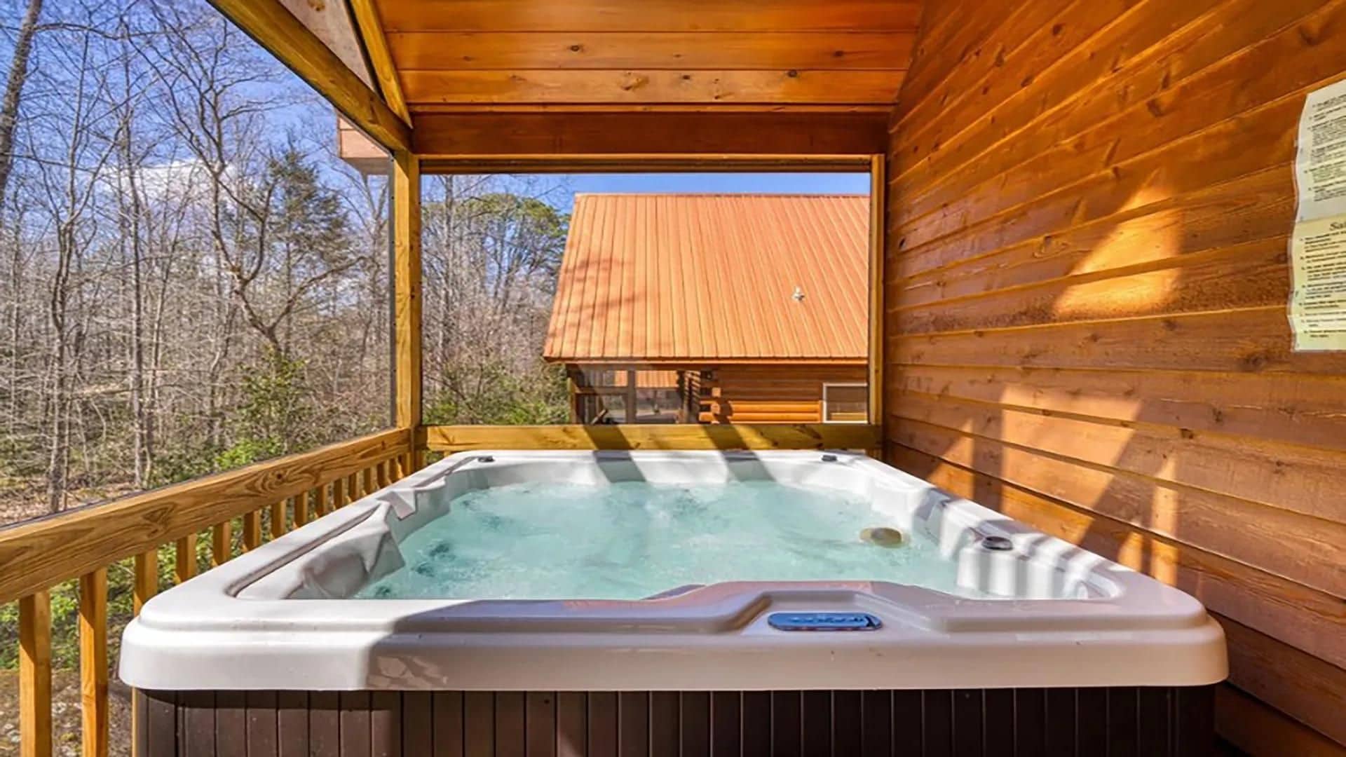 Un jacuzzi en una terraza de madera con vistas a una cabaña al fondo.
