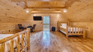 Une cabane avec une chambre à coucher située en mezzanine, un bureau avec deux chaises et une fenêtre donnant sur un paysage enneigé.